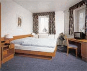 zeigt ein Hotelzimmer mit Doppelbett, Schreibtisch und Fernseher